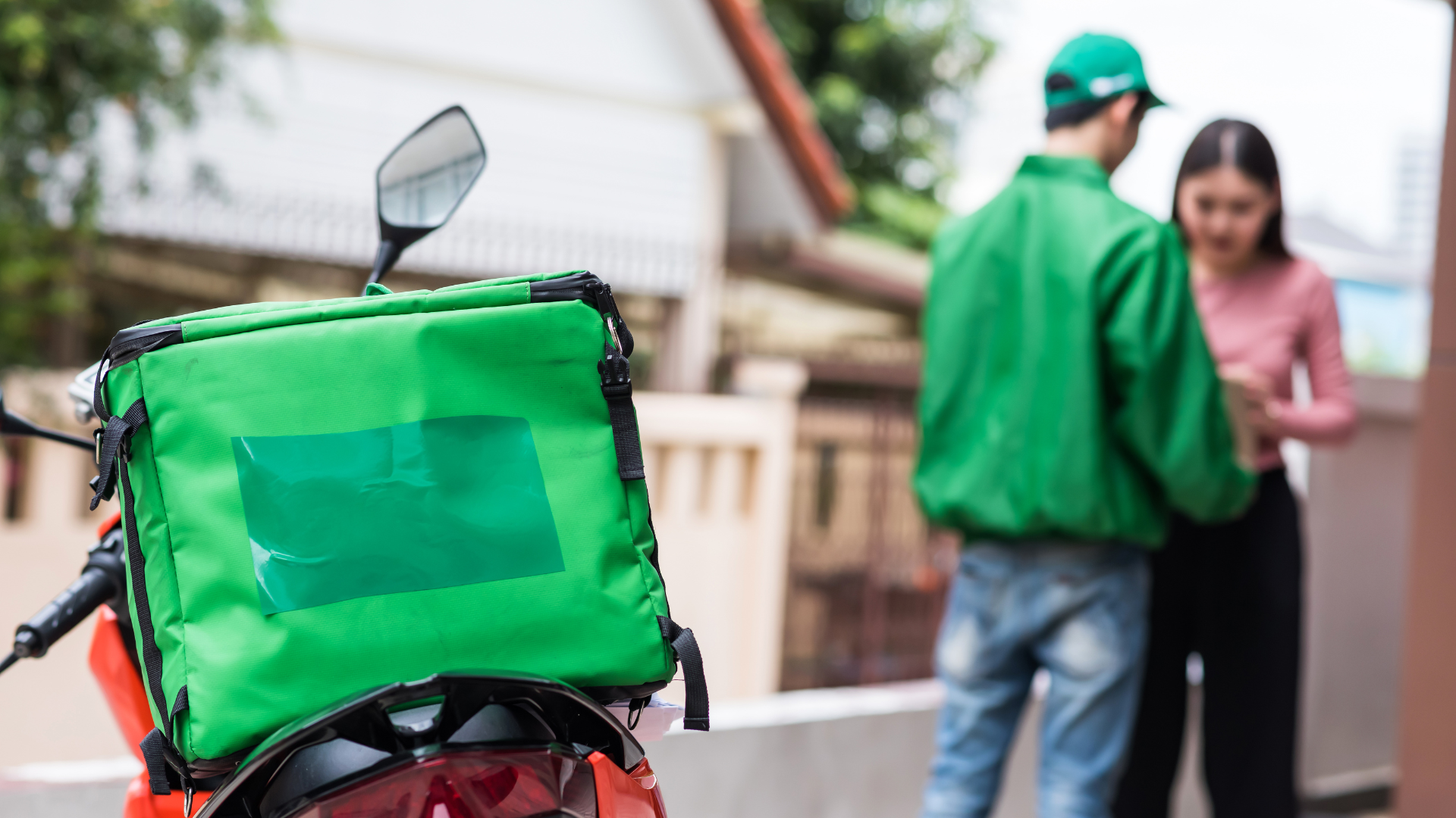 Green food delivery motorvehicle with the food delivery man speaking to the customer in the background about payment.